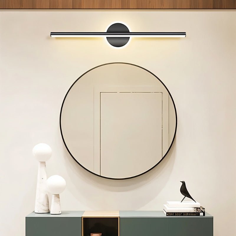 Clérachic black bar wall light above a round black-framed mirror, with a green console, white vases and a bird figure.