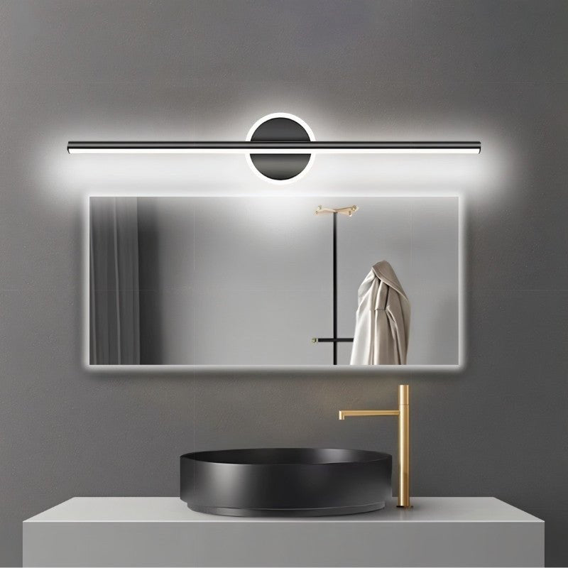 Clérachic black bar wall light lit cool white above a wide backlit mirror, a black basin and a gold tap.