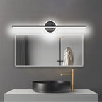 Clérachic black bar wall light lit cool white above a wide backlit mirror, a black basin and a gold tap.
