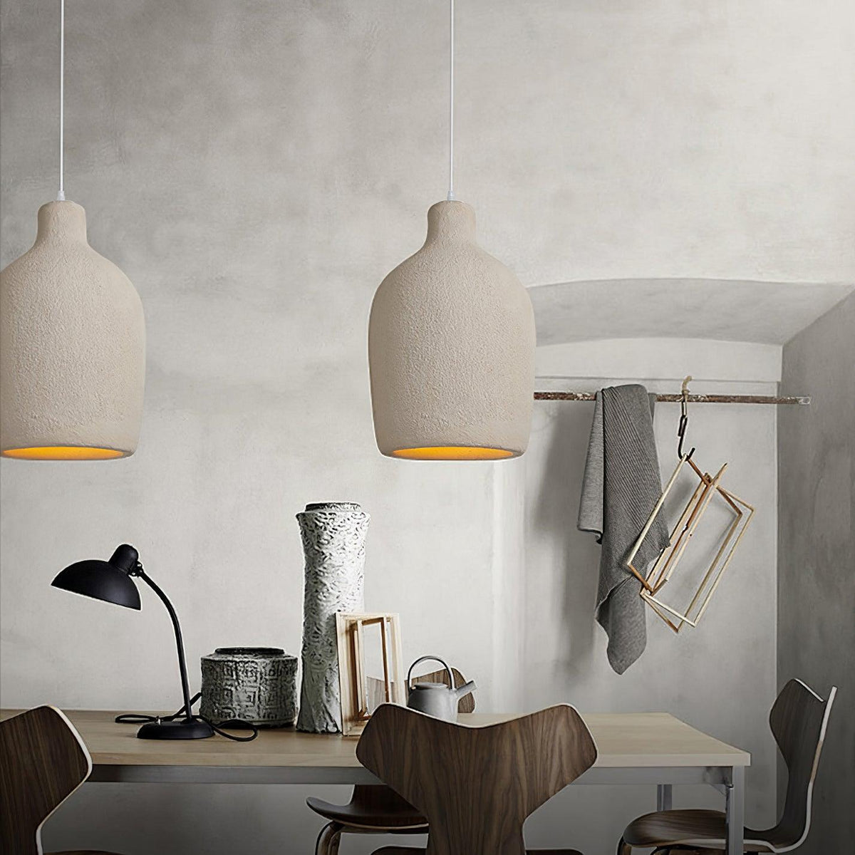Two rounded beige Clérachic pendant lights above a desk with a black desk lamp, a tall grey vase and a hanging blanket.