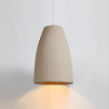 Beige tapered Clérachic pendant light with a warm amber glow spilling down onto a pale grey wall.
