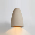 Beige tapered Clérachic pendant light with a warm amber glow spilling down onto a pale grey wall.