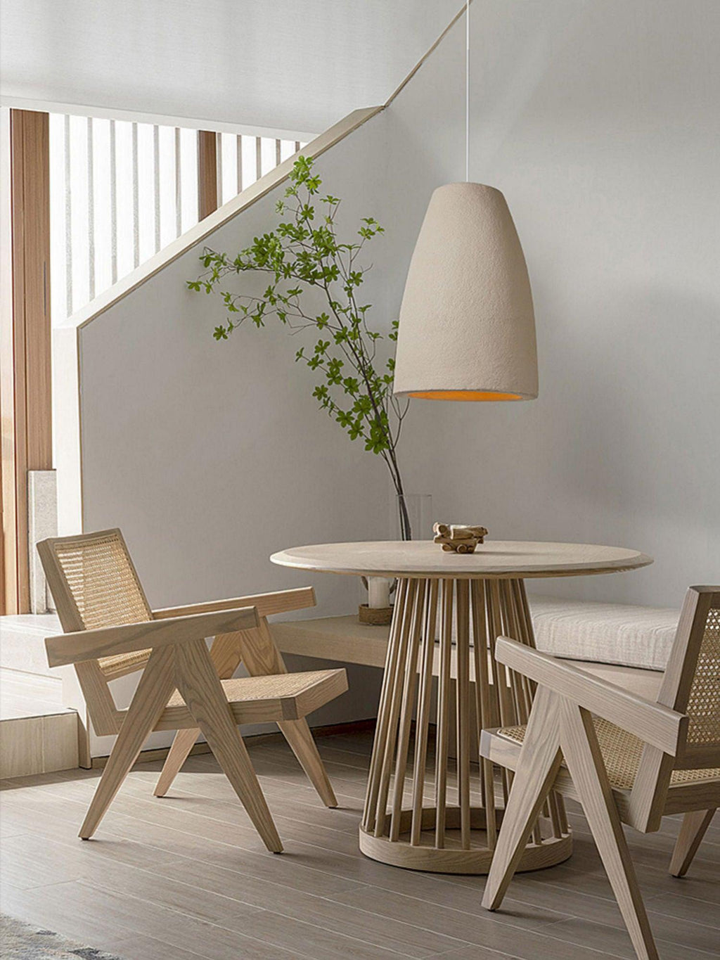 This Clérachic pendant light hangs in a tapered bell shape above a round table, with cane chairs and a staircase behind.