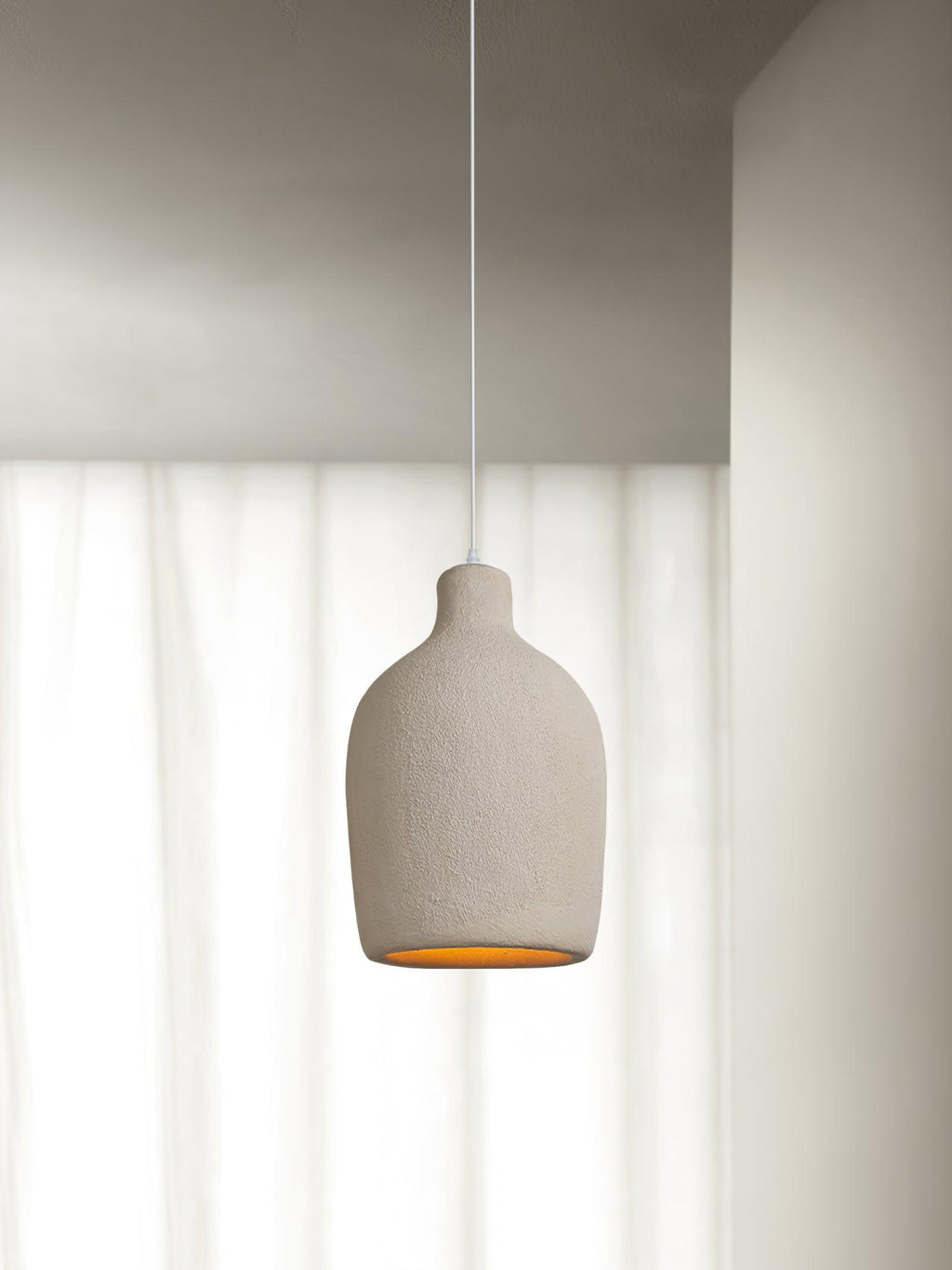 Rounded beige Clérachic pendant light in front of white curtains, with a softly glowing opening and a thin white cable.