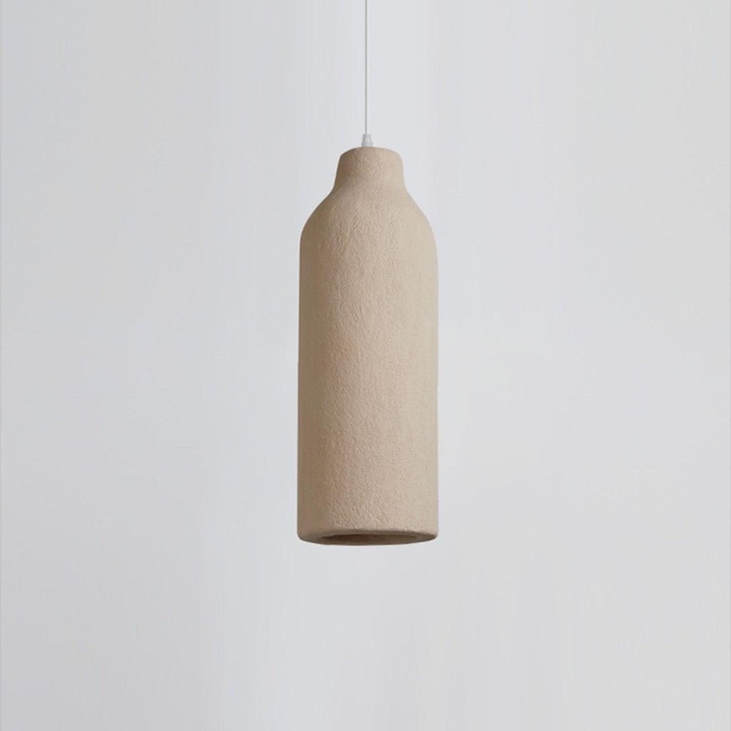 Close view of a slim bottle-shaped Clérachic pendant light with a rough beige surface, on a pale grey backdrop.