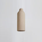 Close view of a slim bottle-shaped Clérachic pendant light with a rough beige surface, on a pale grey backdrop.