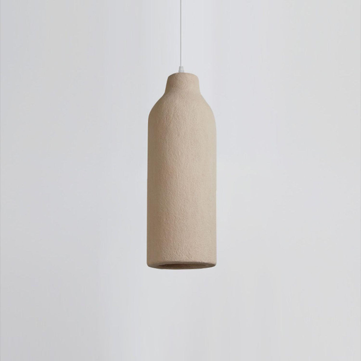 Close view of a slim bottle-shaped Clérachic pendant light with a rough beige surface, on a pale grey backdrop.