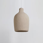 A wide, rounded Clérachic pendant light in a rough beige finish, seen side-on against a pale grey backdrop.