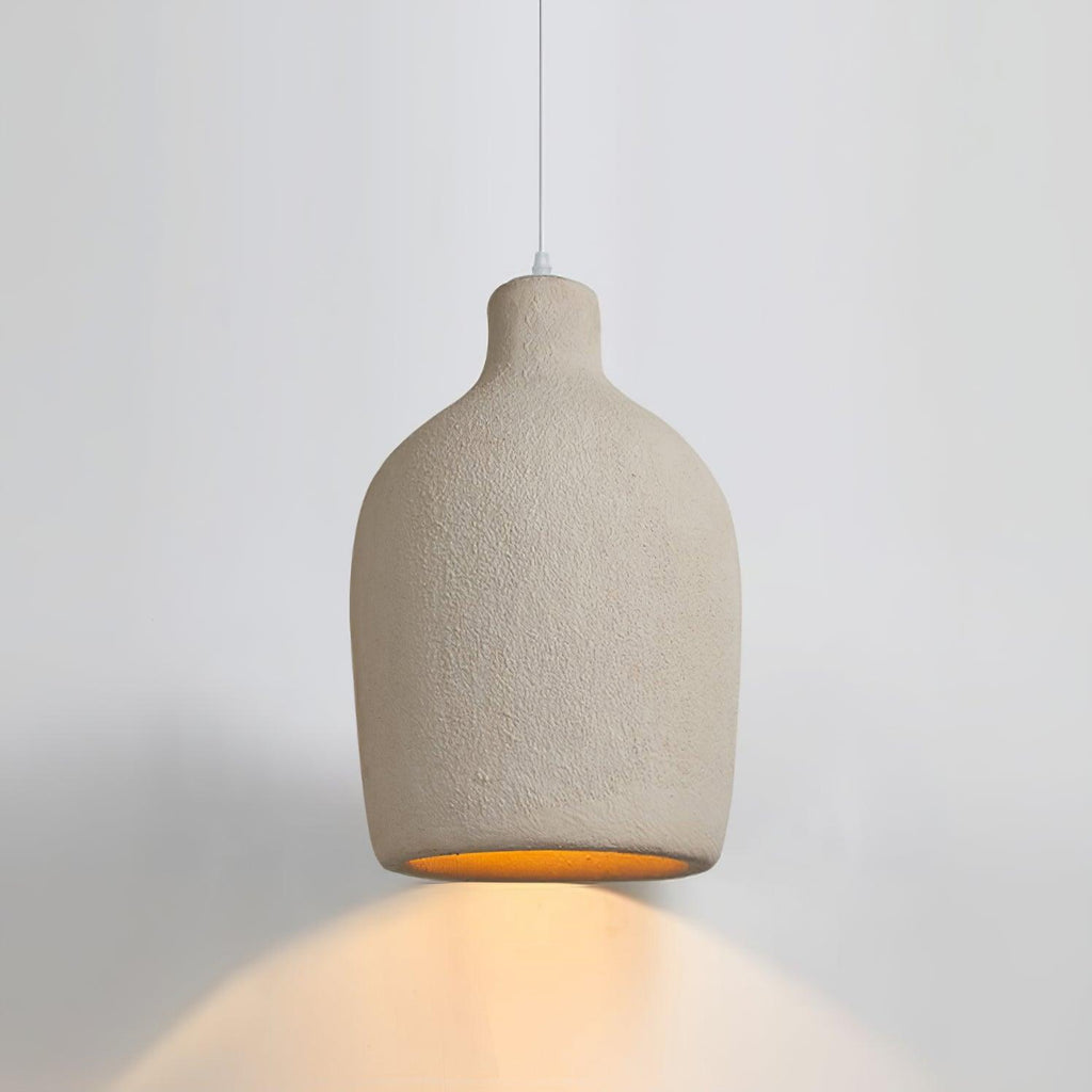 Beige Clérachic pendant light with a rounded body and short neck, casting an amber glow onto the wall behind.