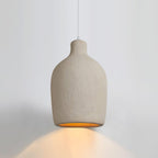 Beige Clérachic pendant light with a rounded body and short neck, casting an amber glow onto the wall behind.