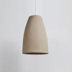 A tapered, bell-shaped Clérachic pendant light in a rough beige finish, on a pale grey backdrop, with its white cable above.
