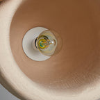 View up inside the shade of a Clérachic pendant light, showing the clear bulb on a white holder and a warm clay-toned interior.