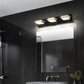 Clérachic three-head black bar light with gold bands and frosted square diffusers, mounted above a mirror in a dark chevron-tiled bathroom.