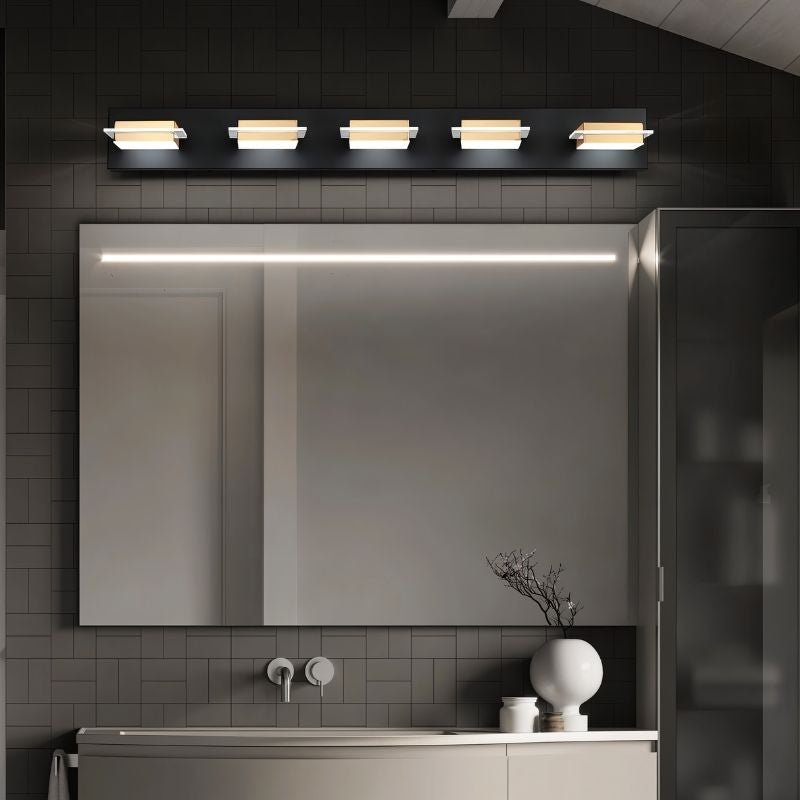 Clérachic five-head black wall bar with gold-toned bands and frosted diffusers, running across a wide vanity mirror in a grey-tiled room.