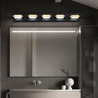 Clérachic five-head black wall bar with gold-toned bands and frosted diffusers, running across a wide vanity mirror in a grey-tiled room.