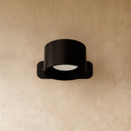 Clérachic compact black round wall lamp with a short drum head, switched off on a warm limewashed wall.