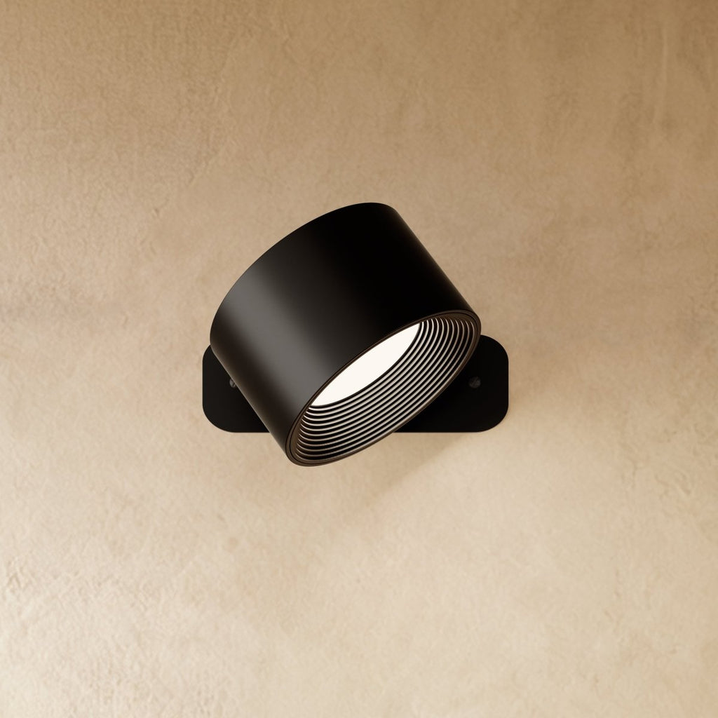 Clérachic black wall lamp with its drum head tilted downward on a slim rounded-corner back plate, lit.