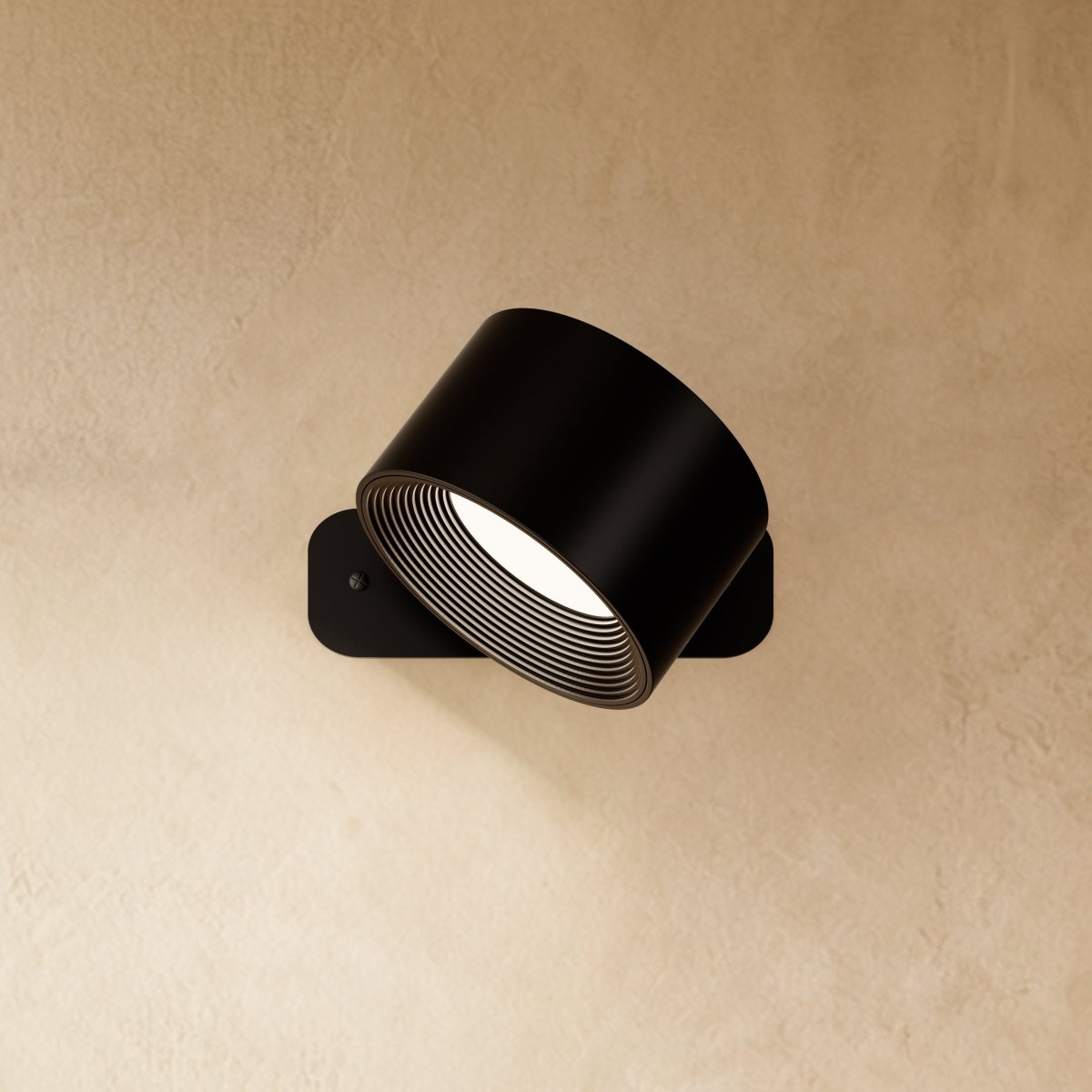 Clérachic black wall lamp with the drum head turned further on its pivot, a ribbed inner ring glowing white.
