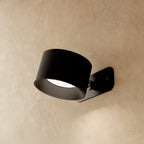 Clérachic black wall lamp seen from the side, its drum head angled down on a small brushed pivot and plate.