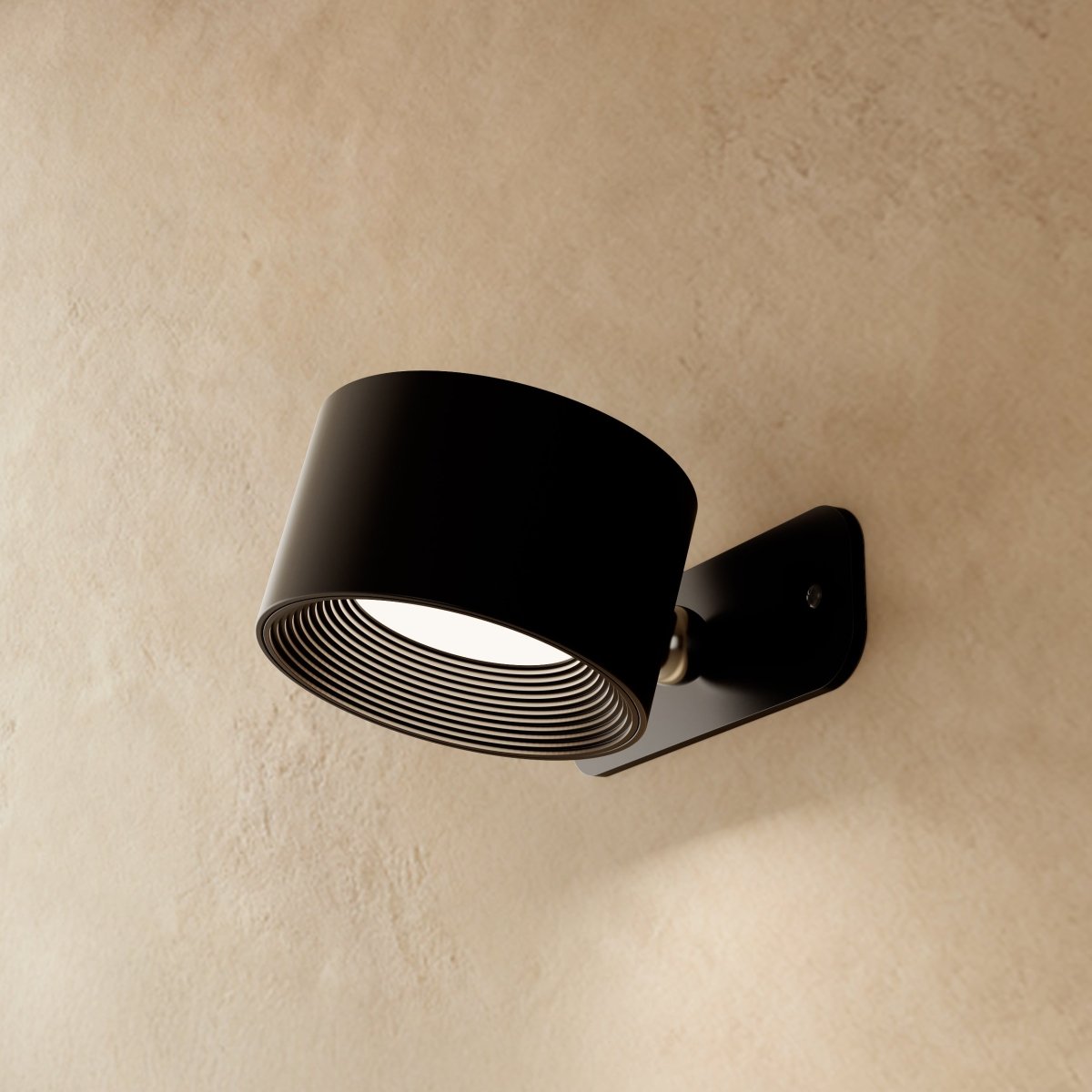 Clérachic black wall lamp seen from the side, its drum head angled down on a small brushed pivot and plate.