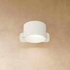 Clérachic compact white round wall lamp with a short drum head, lit, its ribbed inner ring glowing soft white.