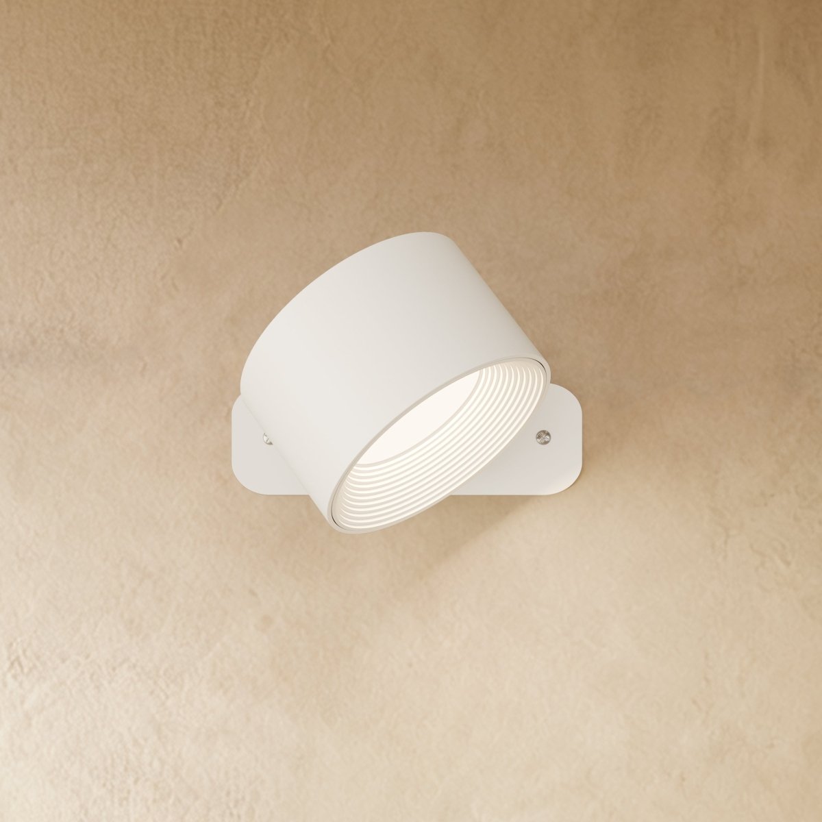 Clérachic white wall lamp with its drum head tilted on a slim rounded-corner back plate, lit.