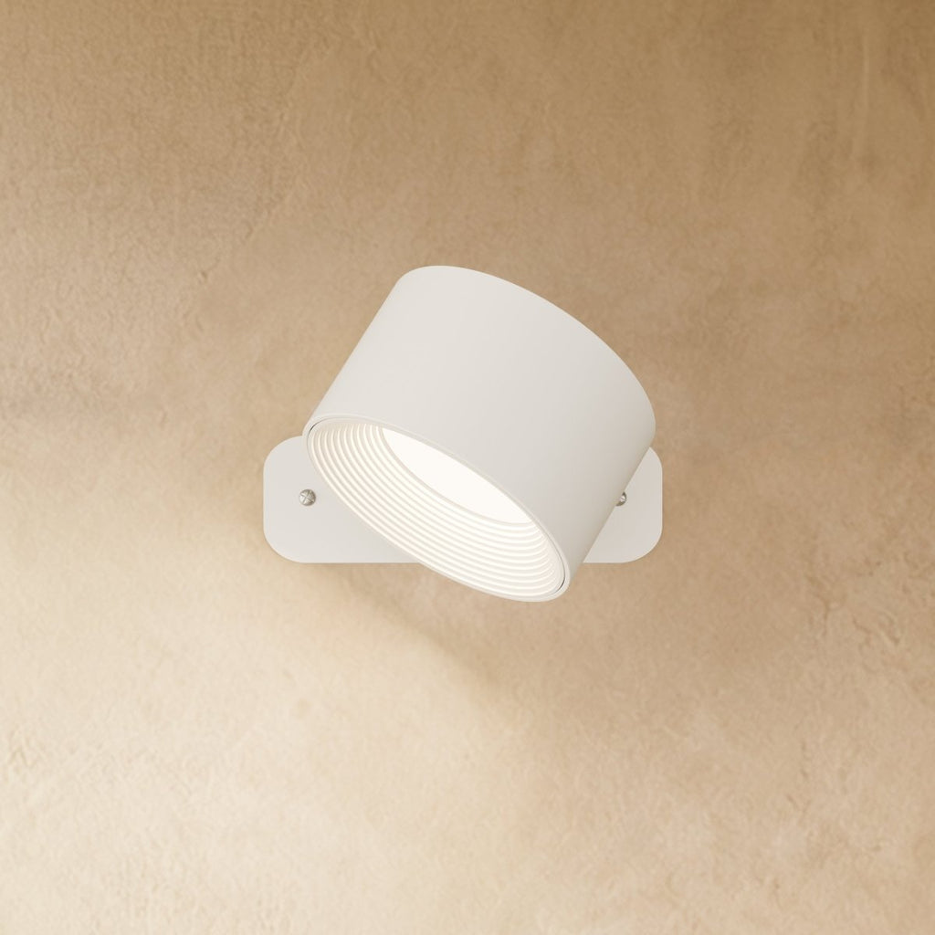 Clérachic white wall lamp with the drum head angled down on its pivot, a ribbed inner ring glowing white.
