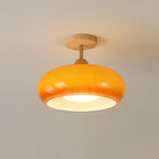 Clérachic Bauhaus glass disc ceiling light in amber orange, lit on a warm taupe ceiling above its round wooden canopy.