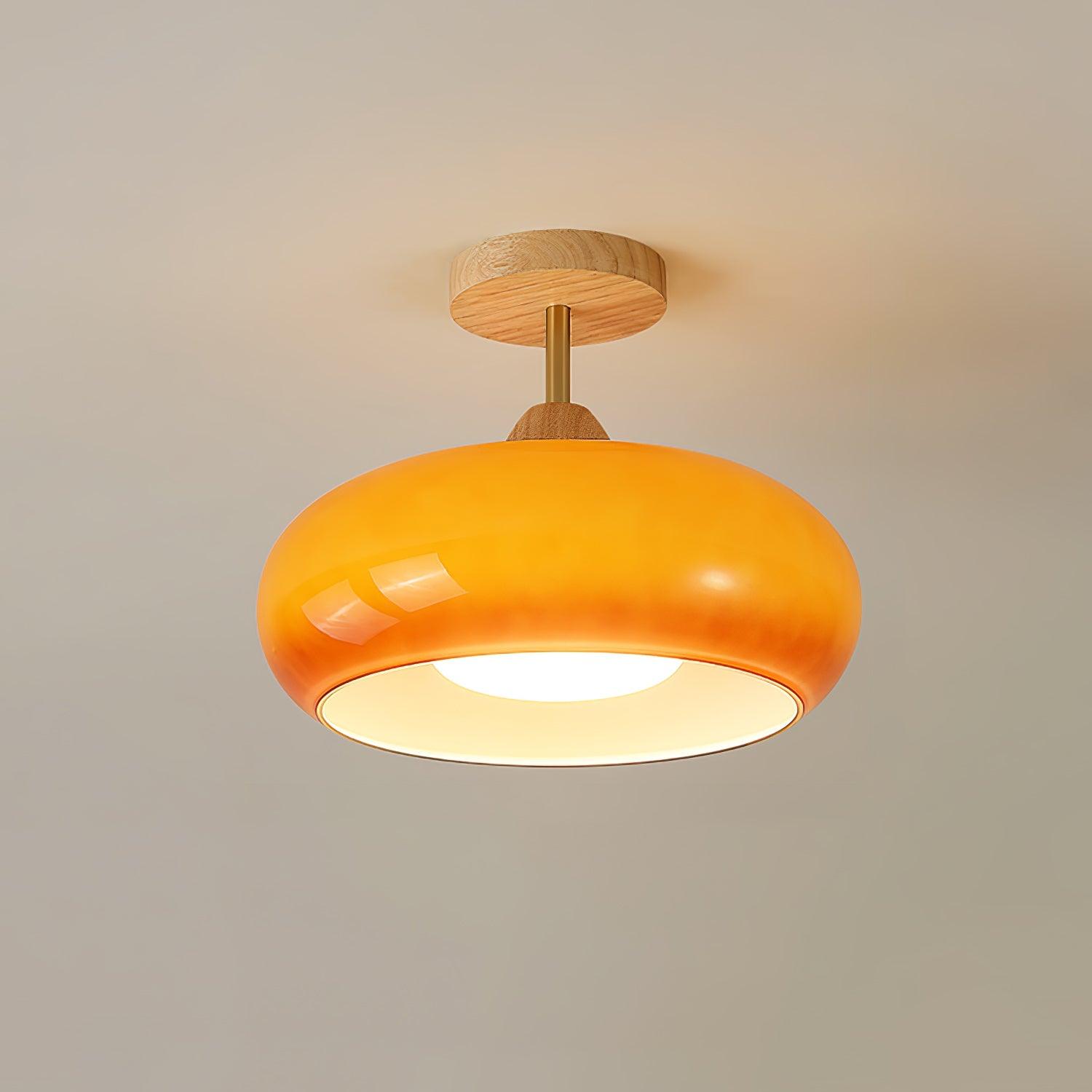 Clérachic Bauhaus glass disc ceiling light in amber orange, lit on a warm taupe ceiling above its round wooden canopy.