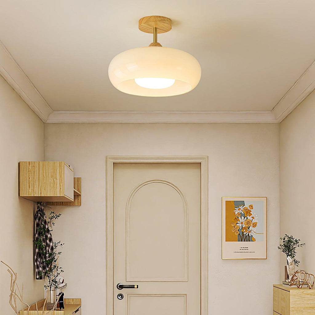 Clérachic Bauhaus glass disc ceiling light in white, lit close to the ceiling of a cream entryway above the front door.
