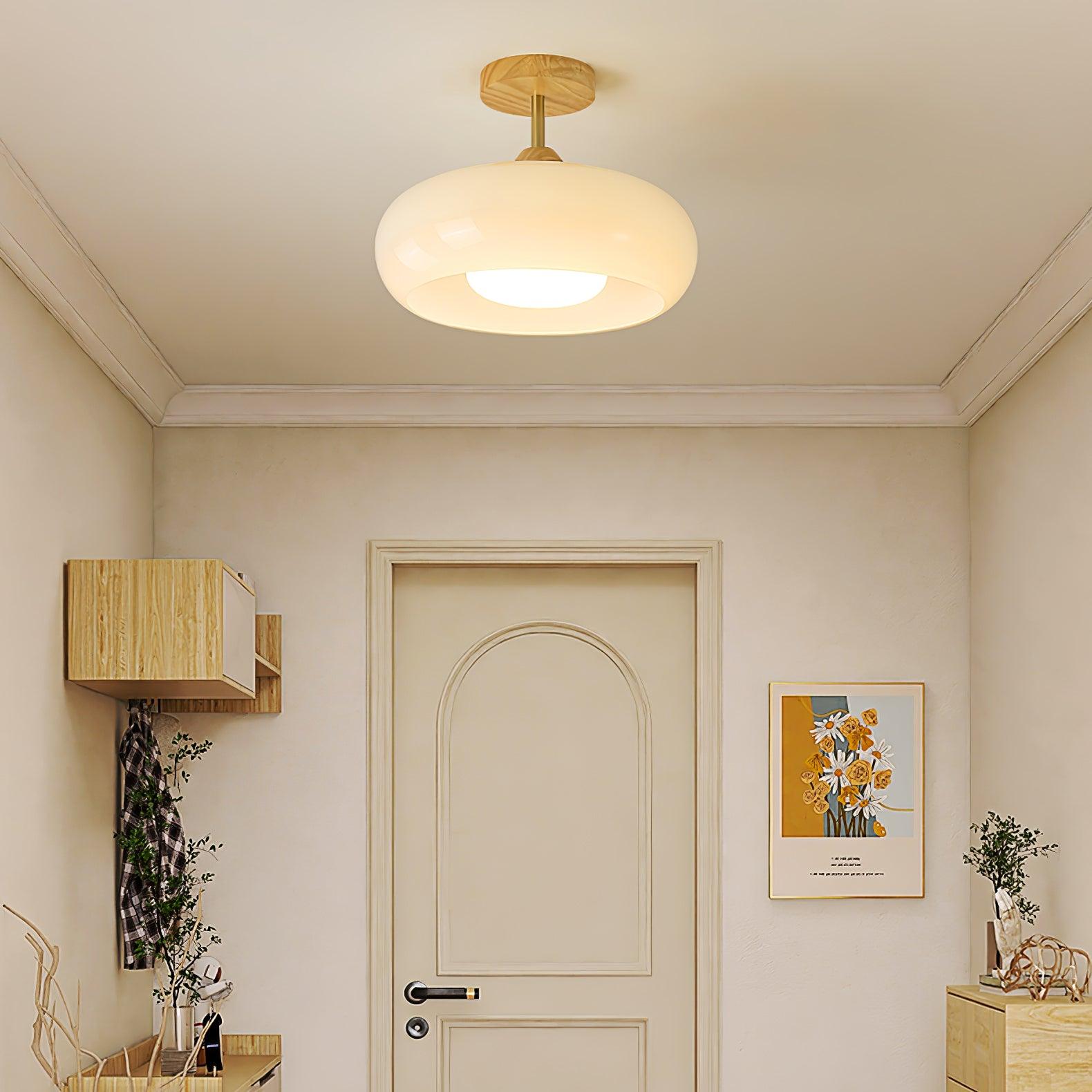 Clérachic Bauhaus glass disc ceiling light in white, lit close to the ceiling of a cream entryway above the front door.