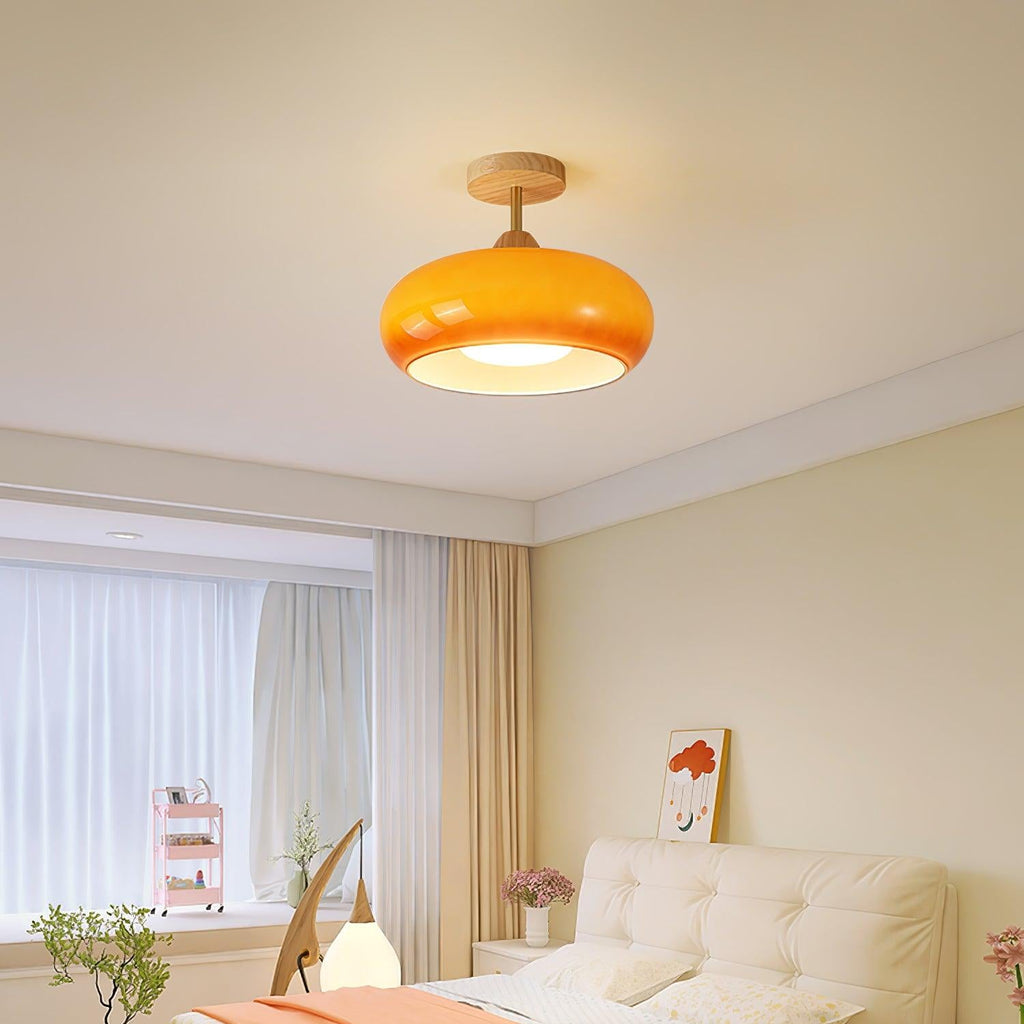 Clérachic Bauhaus glass disc ceiling light in orange, warming a soft cream bedroom above the bed and window curtains.