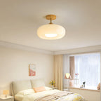 Clérachic Bauhaus glass disc ceiling light in cream white, lighting a bedroom with a bay window and pale headboard.