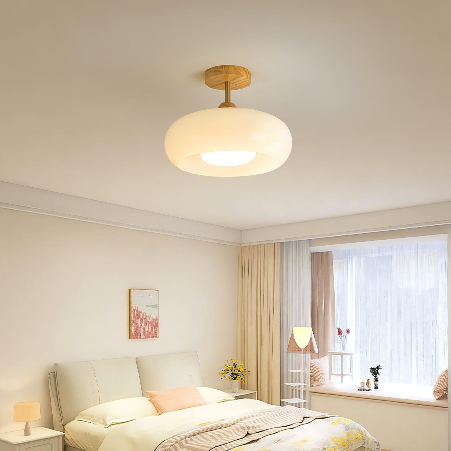 Clérachic Bauhaus glass disc ceiling light in cream white, lighting a bedroom with a bay window and pale headboard.
