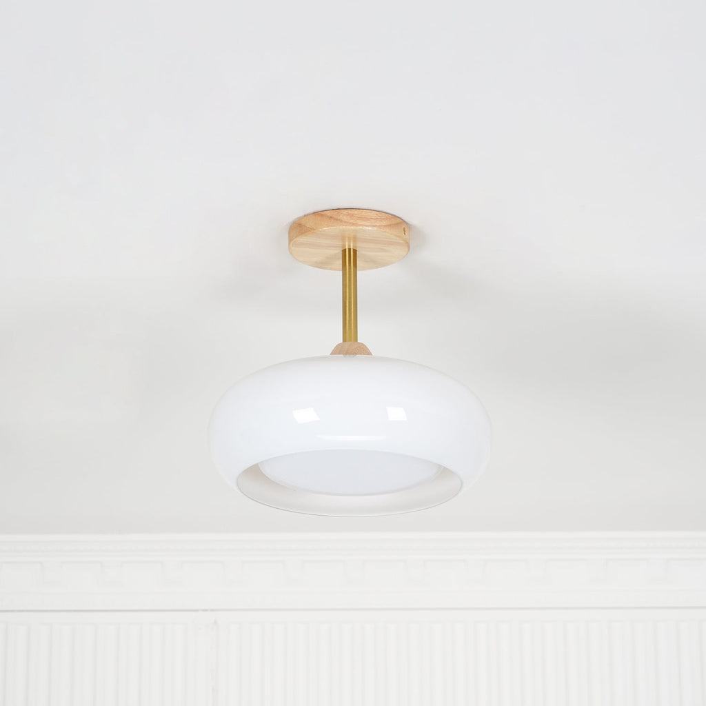 Clérachic Bauhaus glass disc ceiling light in white glass, unlit, showing the brass stem and wood canopy in daylight.