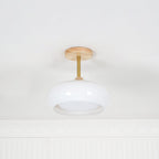 Clérachic Bauhaus glass disc ceiling light in white glass, unlit, showing the brass stem and wood canopy in daylight.