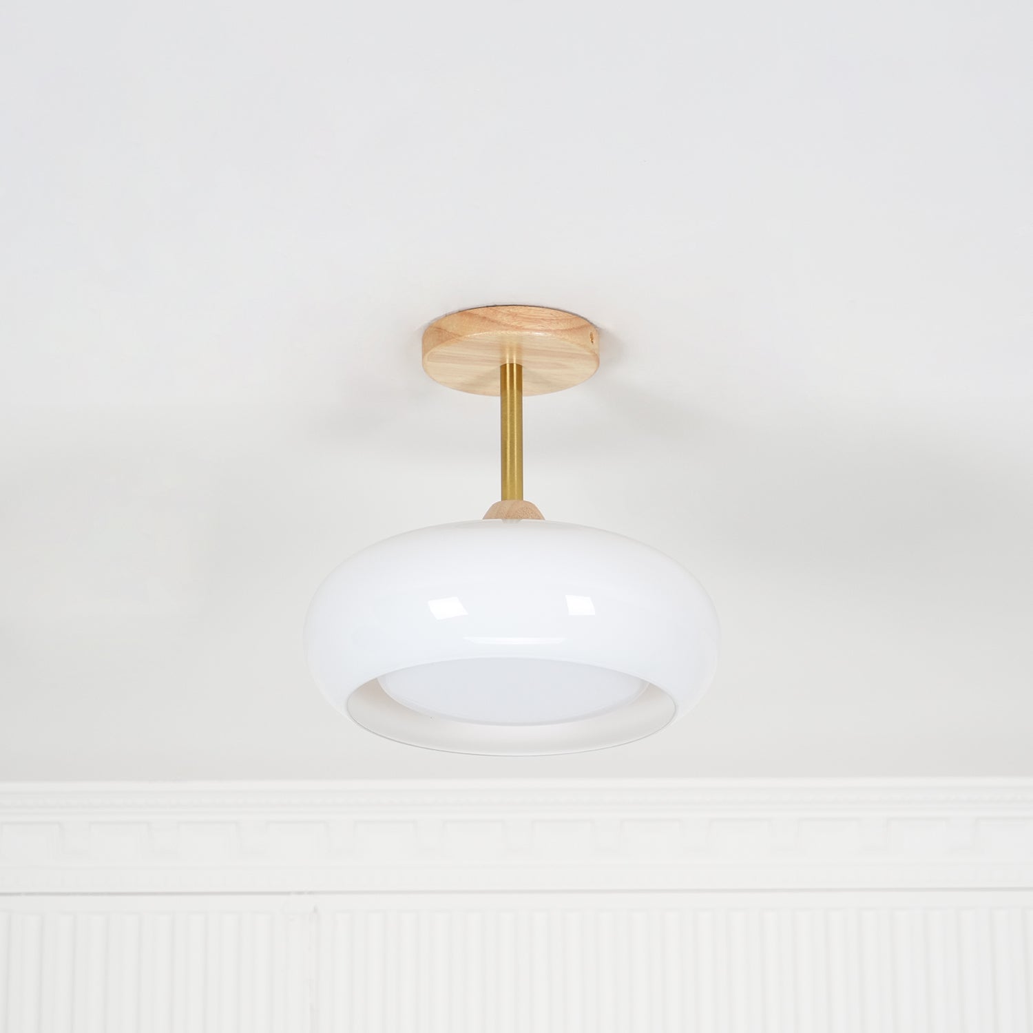 Clérachic Bauhaus glass disc ceiling light in white glass, unlit, showing the brass stem and wood canopy in daylight.