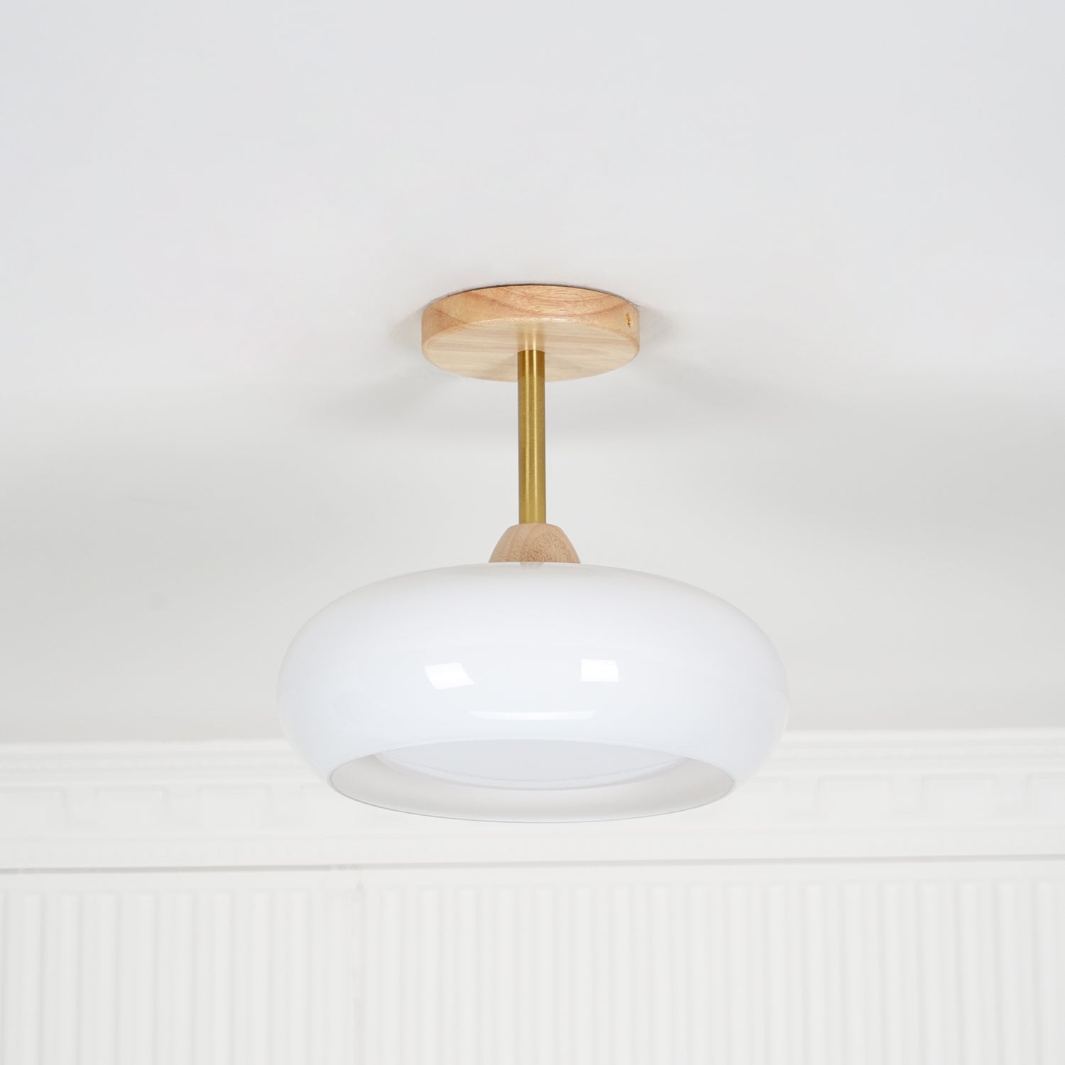 Front view of the Clérachic Bauhaus glass disc ceiling light unlit, its slim brass stem clear against a white wall.