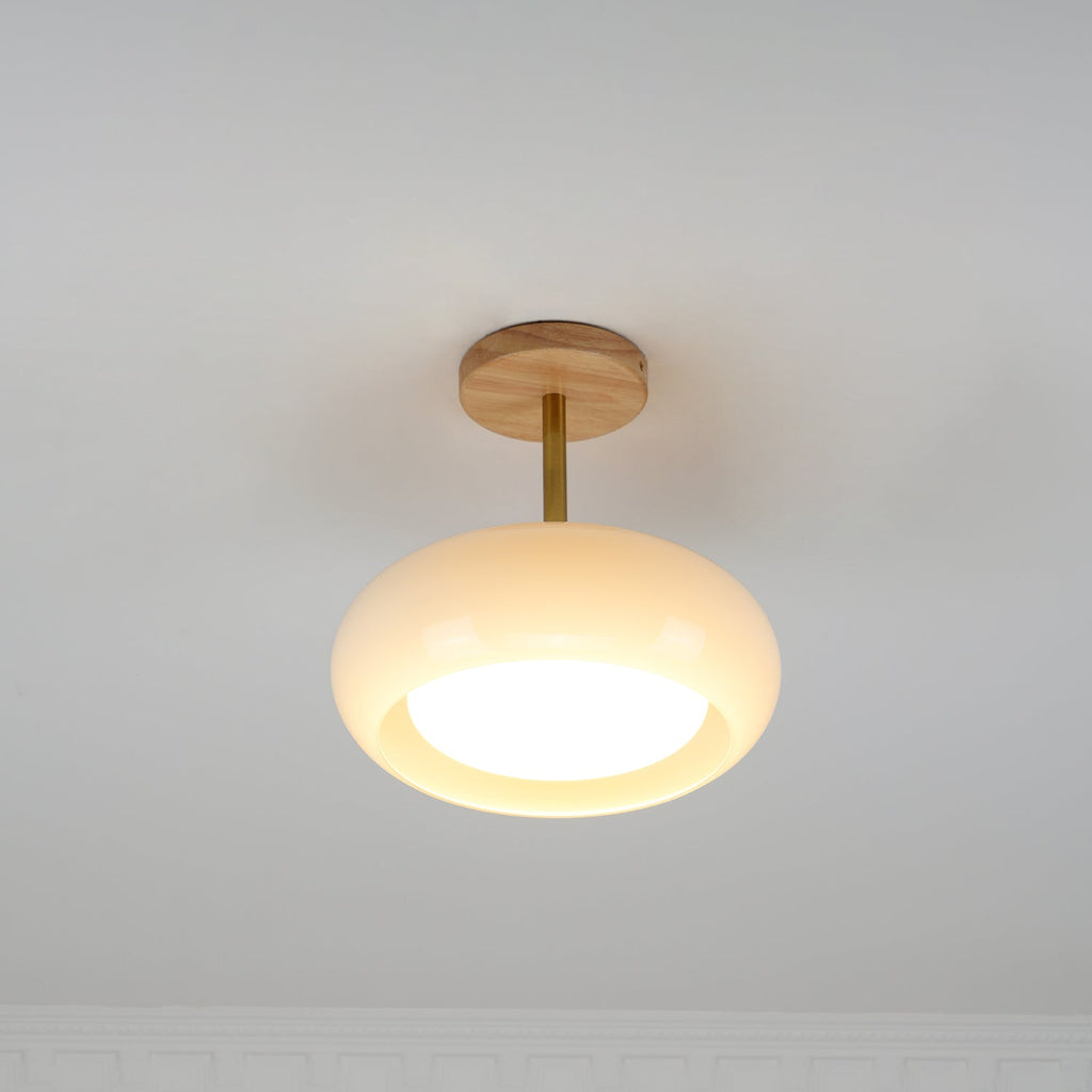 Clérachic Bauhaus glass disc ceiling light lit in a corner, its cream glass throwing a warm pool straight downward.