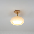 Clérachic Bauhaus glass disc ceiling light lit in a corner, its cream glass throwing a warm pool straight downward.