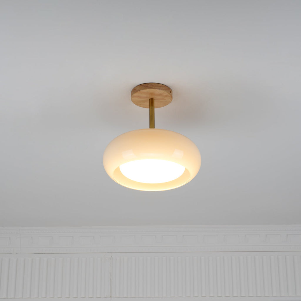 Clérachic Bauhaus glass disc ceiling light mounted semi-flush on a white ceiling, lit above a panelled wall.