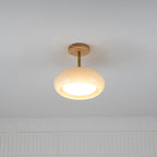 Clérachic Bauhaus glass disc ceiling light mounted semi-flush on a white ceiling, lit above a panelled wall.
