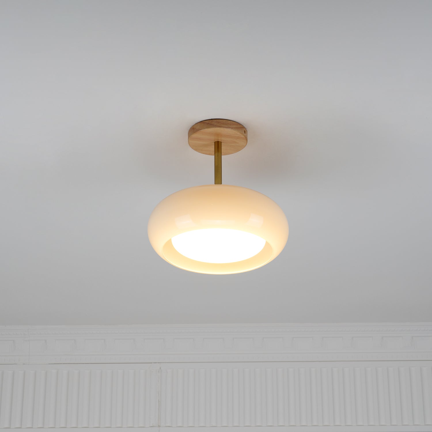 Clérachic Bauhaus glass disc ceiling light mounted semi-flush on a white ceiling, lit above a panelled wall.