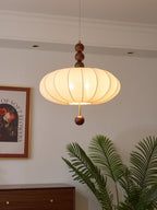 Clérachic ribbed fabric pendant light lit and seen from below, palm fronds framing the lower right of the scene above a walnut sideboard.