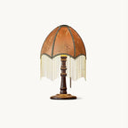 Pleated brown shade trimmed with a beaded fringe on a turned walnut-colour wood base, this Clérachic table lamp on a plain white backdrop.