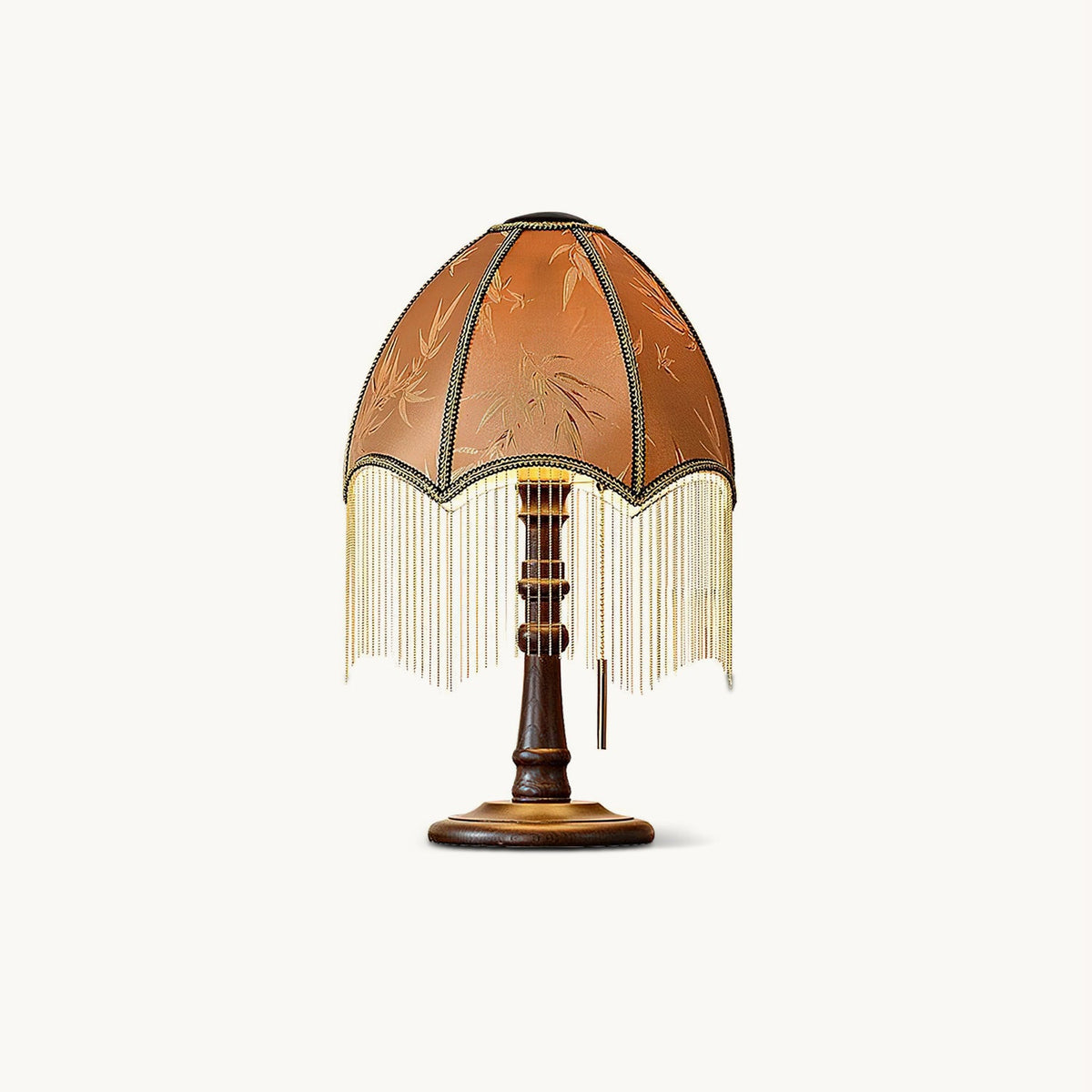 Pleated brown shade trimmed with a beaded fringe on a turned walnut-colour wood base, this Clérachic table lamp on a plain white backdrop.