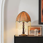 Warm light shines through the brown shade of this Clérachic lamp, its beaded fringe hanging above a sideboard and a framed abstract landscape.