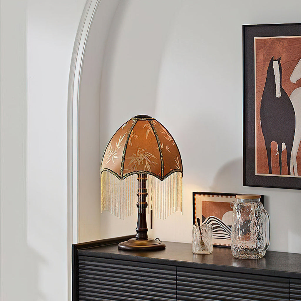 From a lower angle, the beaded-fringe lamp from Clérachic stands on a dark ribbed cabinet in an arched white alcove beside a framed horse artwork.