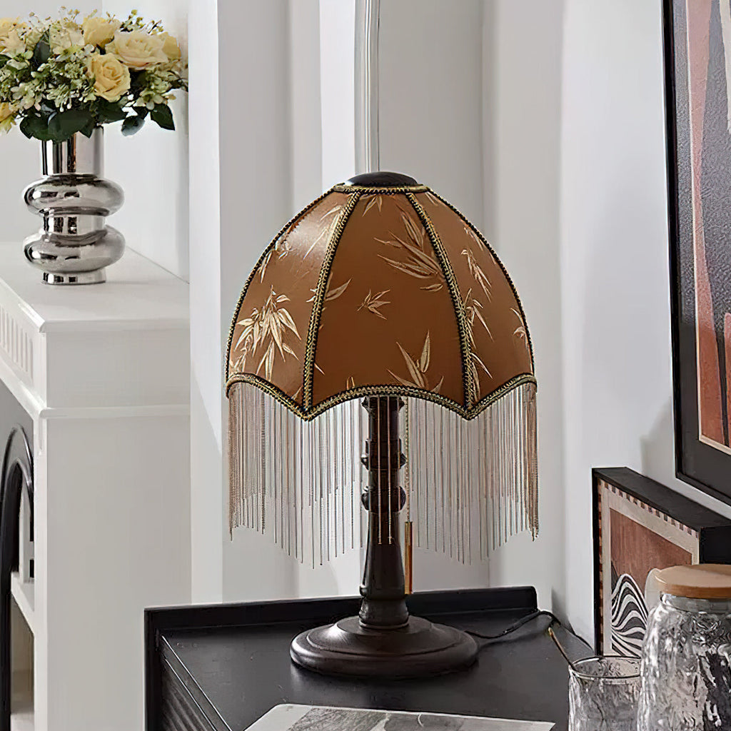 Close to the shade, the leaf-patterned brown fabric and long beaded fringe of this Clérachic lamp, with a silver vase of flowers behind.
