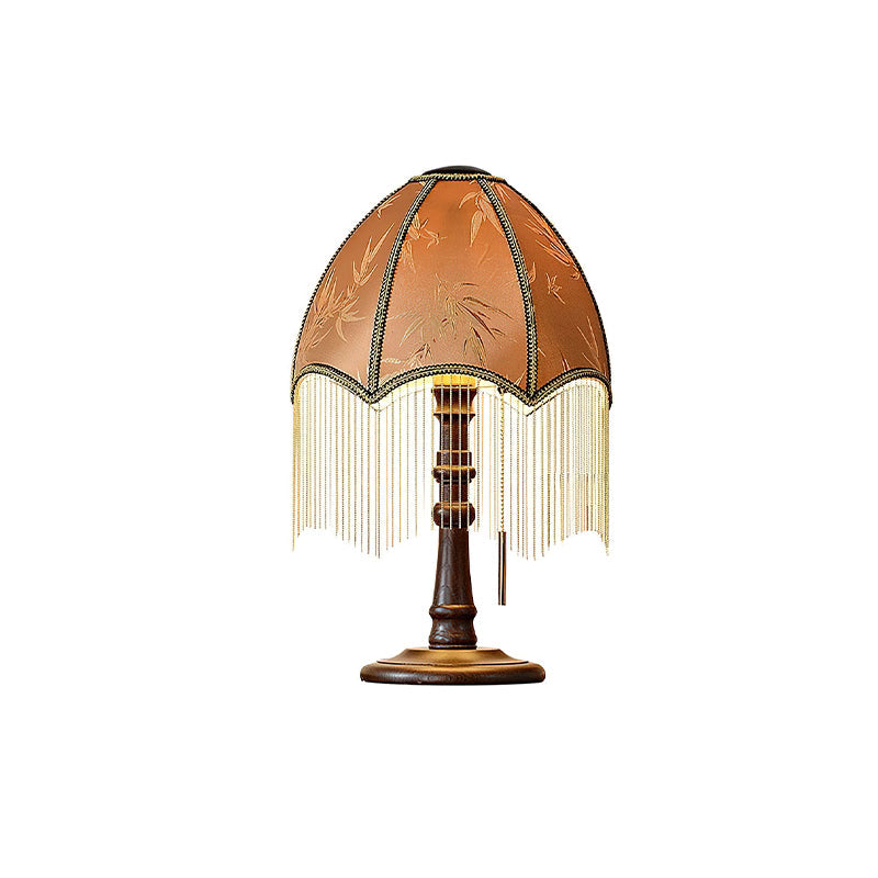 Unlit, this Clérachic table lamp shows its leaf-patterned shade, a fringe of fine beads and a turned wooden stem on a white background.